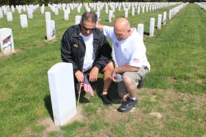Mike Giglio, left, places a flag at his parents’ grave as Bill Parente comforts him.