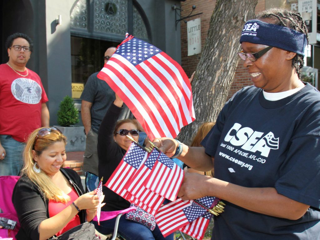 CSEA member Angel Pride, SODEXO at Monroe Community College Local, hands American flags to paradegoers at the annual Labor Day Parade in Rochester.