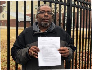 Bronx Psychiatric Center Local President Abraham Benjamin stands in front of the Transitional Living Residence holding one of the contracts clients are required to sign and abide by.