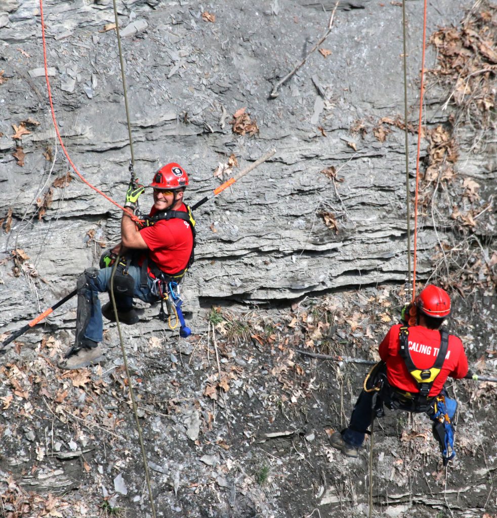 Dustin Karius, left, and Justin Kelly, right, work to knock down loose rocks and debris at Watkins Glen State Park to make the trail below the cliff side safer for the public.