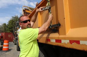 Corey Tilley, a heavy equipment operator at the Town of Queensbury, tightens down a strap on a truck at the town garage.