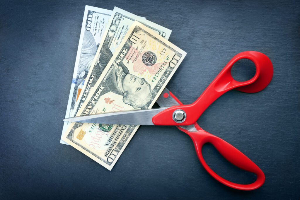 Red scissors cut money on black background.