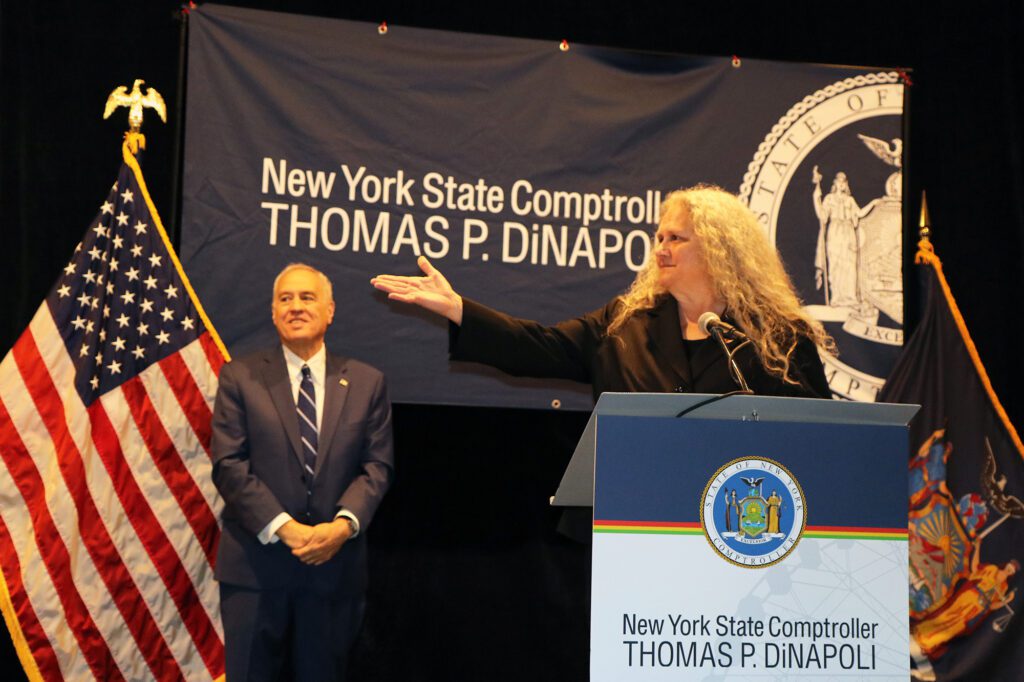 Woman_standing_at_podium_with_arm_stretched_with_man_standing_behind