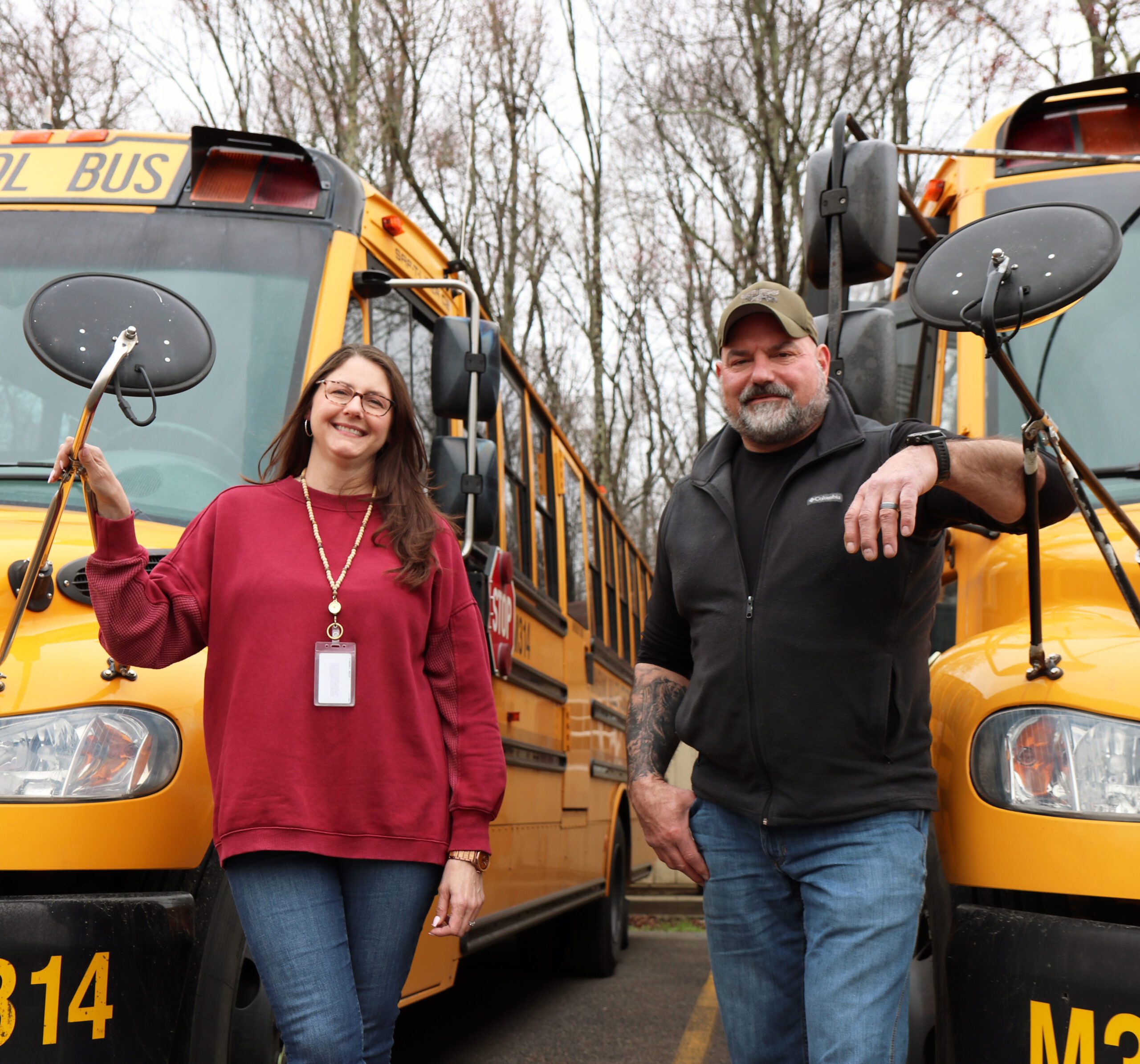 Woman_and_man_standing_in_front_of_two_school_buses